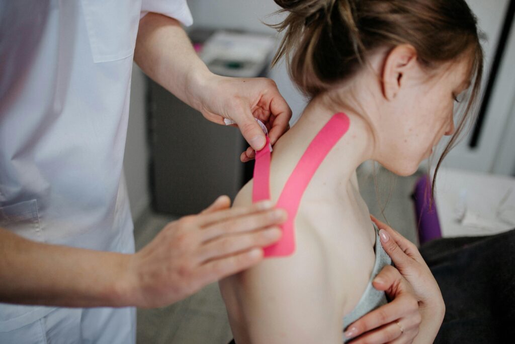 A physiotherapist applies kinesio tape to a woman's shoulder for pain relief and treatment.